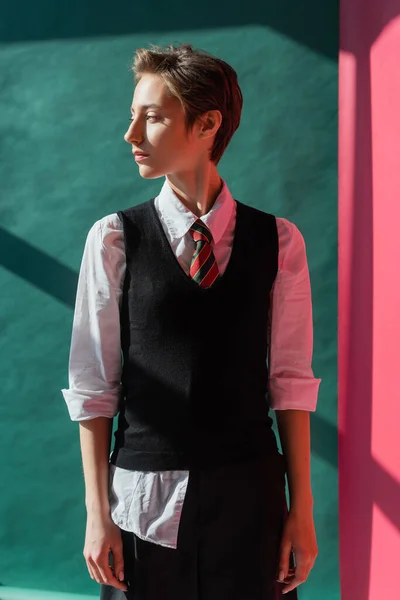 Stylish student with short hair standing in school uniform on pink and green — Stock Photo