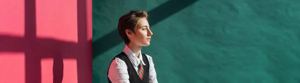 Stylish young woman with short hair posing in school uniform on green and pink background with shadows, banner — Stock Photo