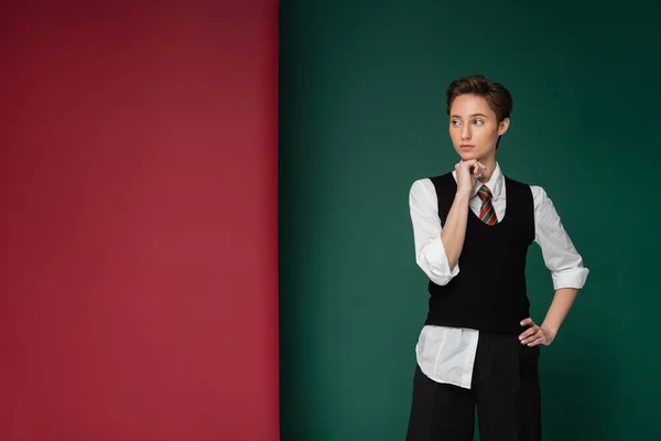 Stylish young student with short hair posing with hand on hip on green and maroon background — Stock Photo