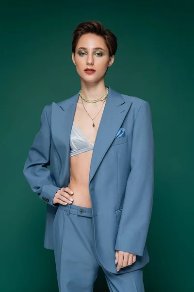 Stylish woman in satin bra and blue pantsuit posing with hand on hip on turquoise green background — Stock Photo