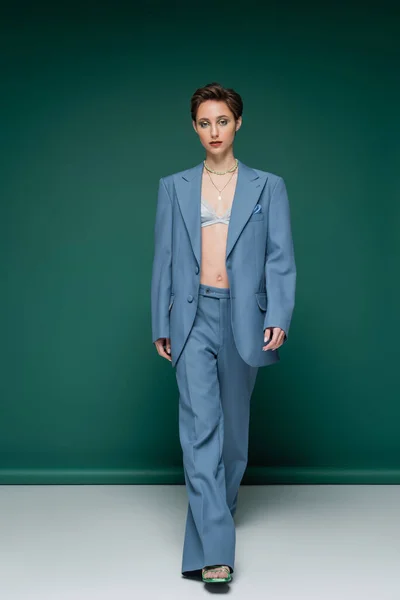 Full length of young woman with short hair walking in blue pantsuit on turquoise green background — Stock Photo