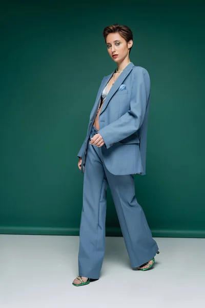 Comprimento total da jovem com cabelo curto andando em pantsuit azul com sutiã em fundo verde-turquesa — Fotografia de Stock