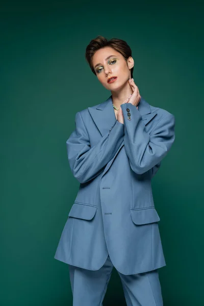 Young woman with short hair posing in blue suit on turquoise green background — Stock Photo