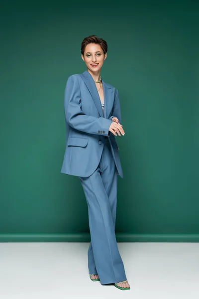 Full length of cheerful young woman with short hair posing in blue suit on turquoise green background — Stock Photo