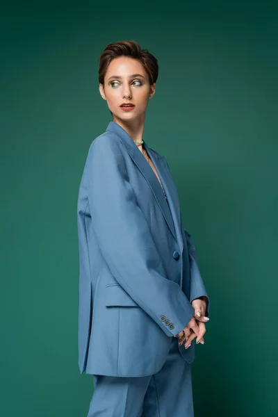 Молодая модель с короткими волосами позирует в синем костюме на бирюзовом зеленом фоне — стоковое фото