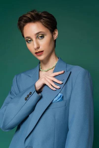 Jeune femme aux cheveux courts posant en blazer bleu et regardant la caméra sur fond vert turquoise — Photo de stock