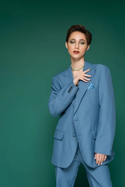 Elegante junge Frau mit kurzen Haaren posiert im blauen Blazer und blickt in die Kamera auf türkisgrünem Hintergrund — Stockfoto