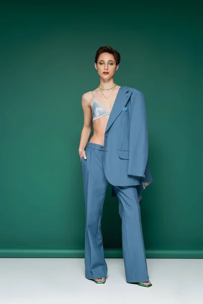 Full length of young model with short hair posing in satin bra with blue blazer on shoulder on turquoise green background — Stock Photo