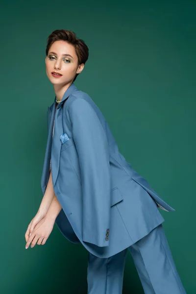 Young woman with short hair posing in blue pantsuit on turquoise background — Stock Photo