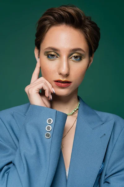 Elegante junge Frau mit kurzen Haaren und hellem Make-up, die isoliert auf Türkis in die Kamera blickt — Stockfoto
