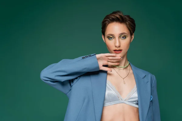 Young woman with short hair posing in blue jacket with satin bra underneath on turquoise green background — Stock Photo