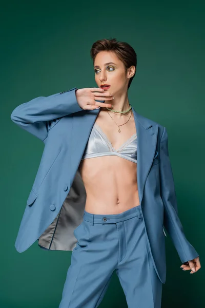 Young woman with short hair posing in blue pants and blazer with satin bra underneath on turquoise background — Stock Photo