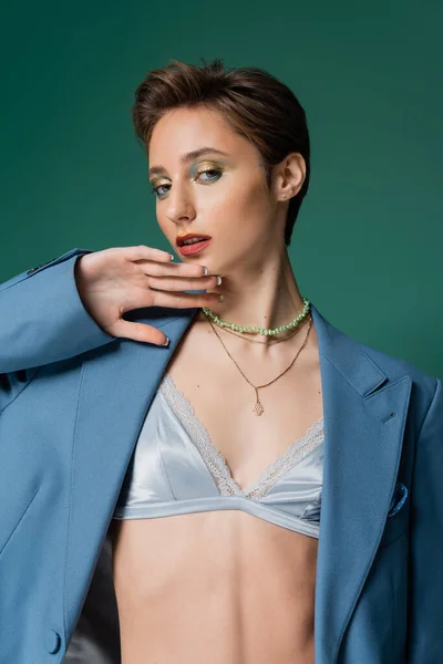 Young woman with short hair posing in blue jacket with silk bra underneath on turquoise background — Stock Photo