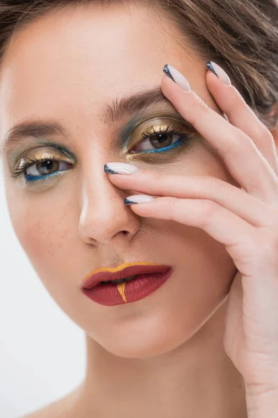 Nahaufnahme einer jungen Frau mit hellem Make-up, die ihr Gesicht berührt und isoliert auf grau schaut — Stockfoto