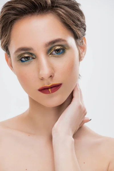 Портрет молодої жінки з яскравим макіяжем, який торкається шиї і дивиться на камеру ізольовано на сірому — Stock Photo