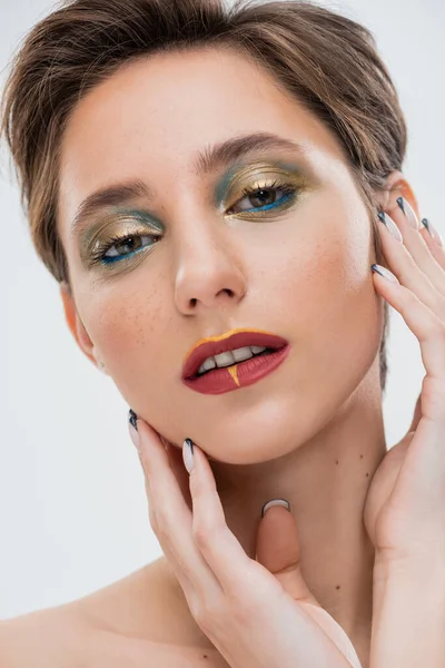 Nahaufnahme einer jungen Frau mit hellem Make-up, die die Wangen berührt und isoliert auf grau schaut — Stockfoto