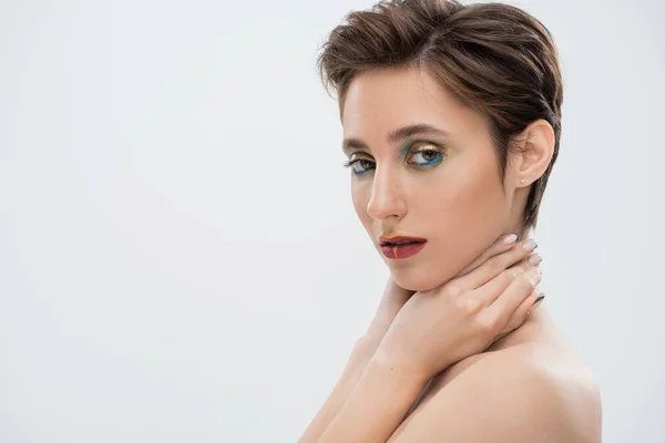 Porträt einer jungen Frau mit hellem Make-up, die den Hals berührt und in die Kamera schaut, isoliert auf grau — Stockfoto