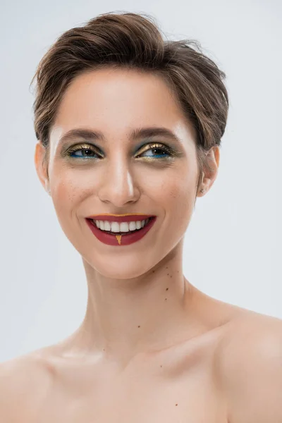 Portrait of cheerful young woman with shiny makeup and short hair isolated on grey — Stock Photo