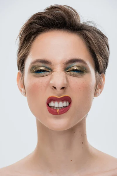 Porträt einer emotionalen jungen Frau mit glänzendem Make-up und kurzen Haaren, die vereinzelt auf grau grinsen — Stockfoto