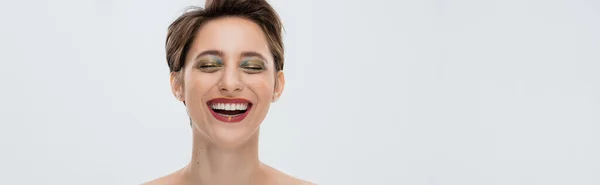 Positive young woman with shiny makeup and short hair smiling isolated on grey, banner — Stock Photo