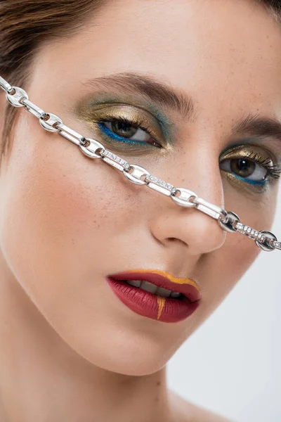 Close up of young woman with shiny eye makeup and silver chain on face isolated on grey — Stock Photo