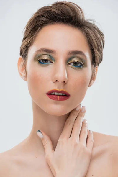Brünette junge Frau mit schimmernden Augen Make-up und roten Lippen berühren Hals isoliert auf grau — Stockfoto