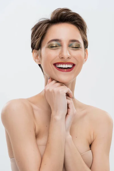 Fröhliche junge Frau mit schimmerndem Augen-Make-up im trägerlosen BH isoliert auf grau — Stockfoto