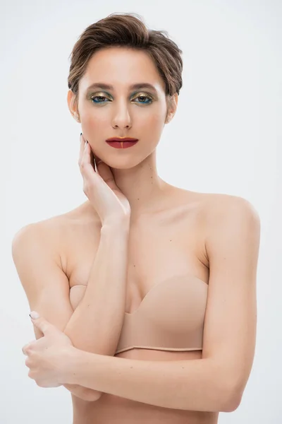 Pretty young woman with shiny eye makeup standing in strapless bra isolated on grey — Stock Photo