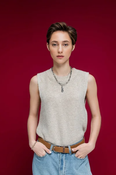Young woman in sleeveless shirt and chain necklace standing on maroon background — Stock Photo
