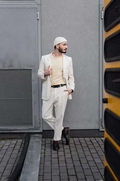 Стильный гей в шляпе и костюме позирует возле здания на городской улице — стоковое фото