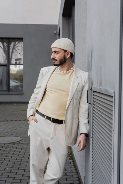 Elegante uomo omosessuale in cappello beige posa vicino al muro di costruzione all'aperto — Foto stock