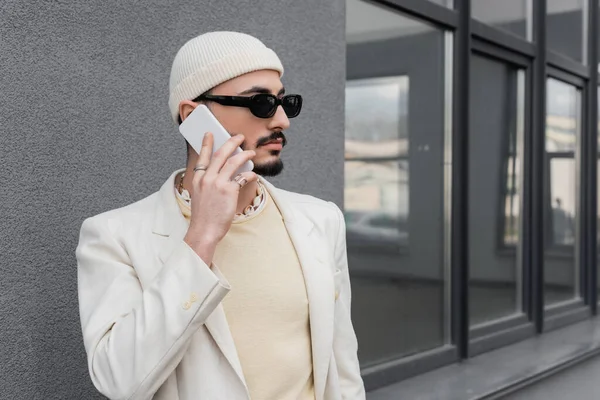 Hombre homosexual de moda en gafas de sol hablando por teléfono móvil en la calle urbana - foto de stock