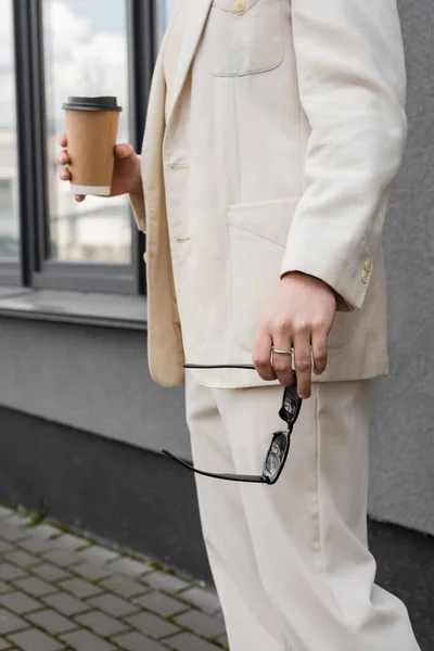 Cropped view of gay man in suit holding sunglasses and coffee to go outdoors — Stock Photo