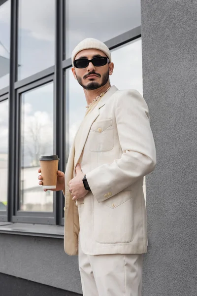 Модний гей-чоловік в сонцезахисних окулярах і капелюсі тримає каву, щоб піти на міську вулицю — стокове фото