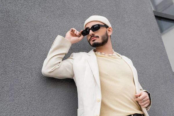 Gut gekleideter Schwuler in Jacke und Hut berührt Sonnenbrille auf urbaner Straße — Stockfoto