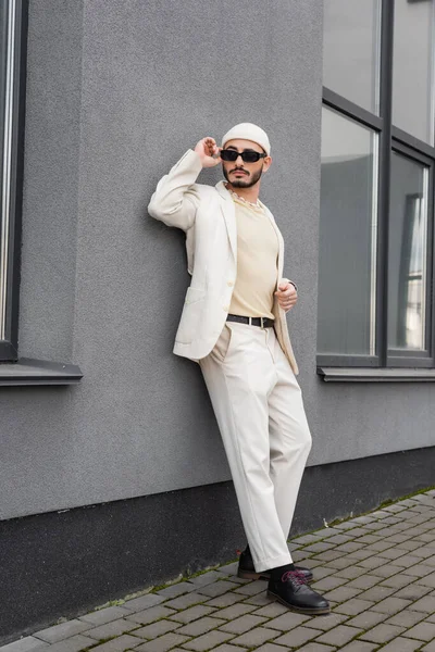 Modischer Schwuler mit Sonnenbrille und beigem Anzug steht in der Nähe von Gebäuden im Freien — Stockfoto