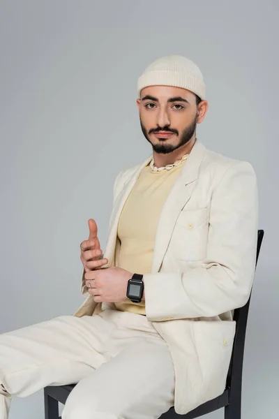 Bearded homosexual man in hat and suit sitting on chair isolated on grey — Stock Photo