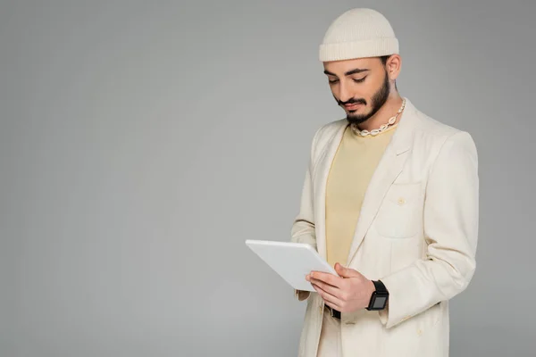 Joven gay hombre en beige traje y sombrero usando digital tablet aislado en gris - foto de stock
