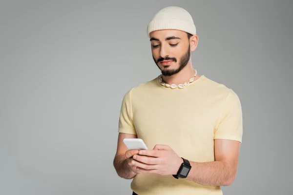 Fashionable gay man in hat using cellphone isolated on grey — Stock Photo