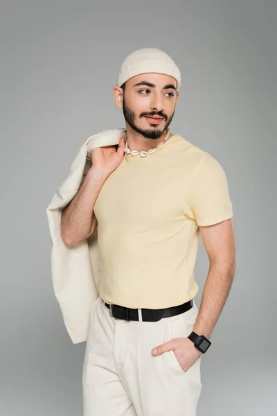 Retrato de elegante gay homem no bege chapéu posando e segurando casaco isolado no cinza — Fotografia de Stock
