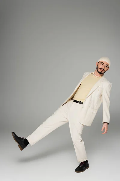 Longitud completa de hombre gay de moda en traje beige mirando hacia otro lado sobre fondo gris - foto de stock