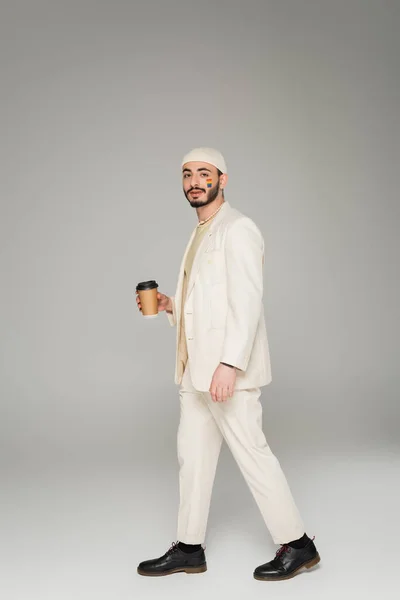 Stilvoller junger schwuler Mann mit lgbt-Fahne auf der Wange mit Kaffee auf grauem Hintergrund — Stock Photo