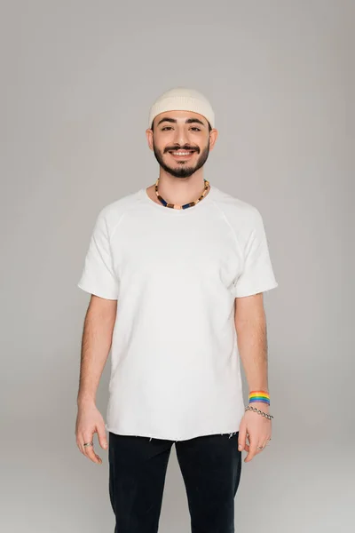 Sorrindo gay homem no chapéu com lgbt pulseira na mão olhando para câmera isolada no cinza — Fotografia de Stock