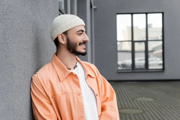 Seitenansicht eines unbeschwerten schwulen Mannes mit Hut, der in der Nähe eines Gebäudes an der Stadtstraße wegschaut — Stockfoto