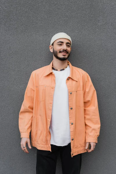 Überglücklicher und bärtiger schwuler Mann mit Hut und Jacke steht neben Mauer im Freien — Stockfoto