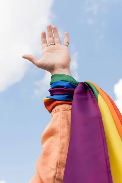 Vista recortada del hombre gay con bandera lgbt en la mano y el cielo en el fondo al aire libre, Día internacional contra la homofobia - foto de stock