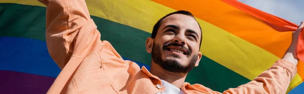 Low angle view of cheerful homosexual man holding lgbt flag outdoors, banner — Stock Photo