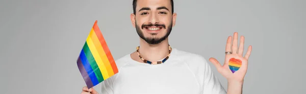Alegre homossexual homem com lgbt bandeira e coração na mão isolado no cinza, bandeira — Fotografia de Stock