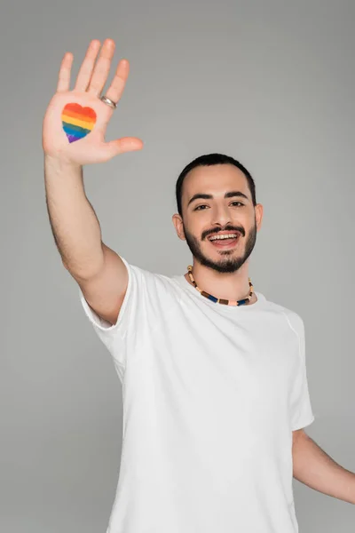 Carefree gay man showing lgbt flag in heart shape on hand isolated on grey, International day against homophobia — Stock Photo