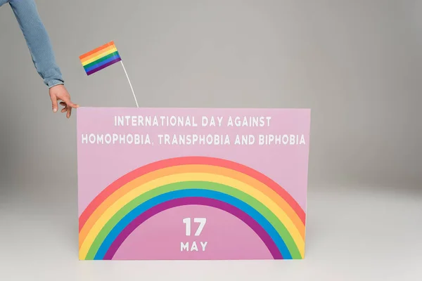 Vista ritagliata dell'uomo gay vicino al cartello con la Giornata internazionale contro omofobia, transfobia e bifobia lettering sul grigio — Foto stock
